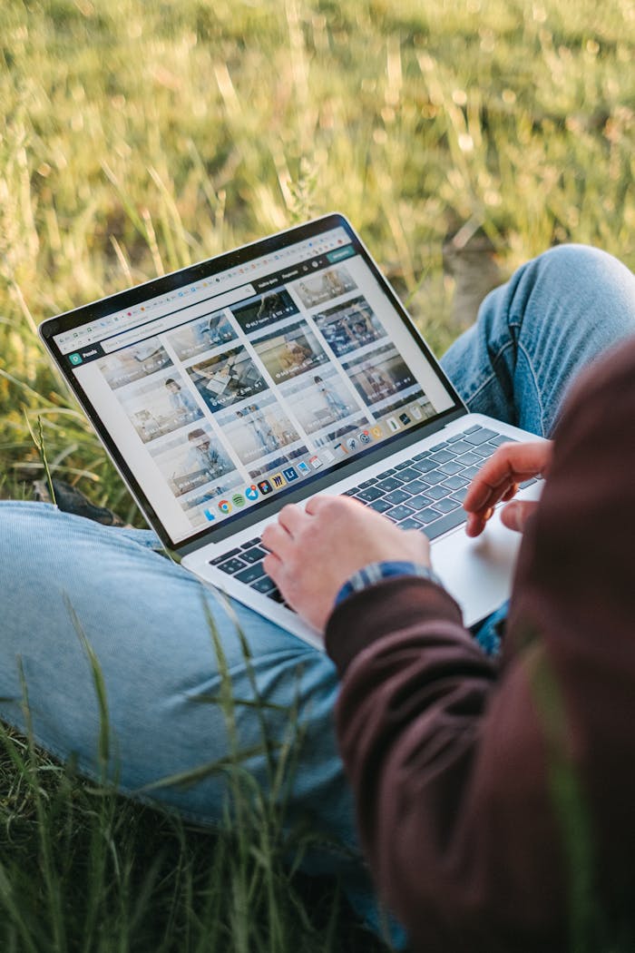A person working remotely on a laptop while sitting on the grass outdoors, showcasing a digital lifestyle.